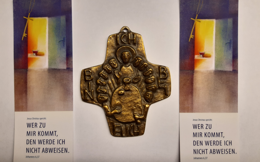 Lesezeichen mit Jahreslosung 2022 - Jesus Christus spricht: Wer zu mir kommt, den werde ich nicht abweisen. Johannes 6,37.
In der Mitte ist eine Art Amulett mit einer Abendmahlsszene und den Worten Ich bin bei euch.