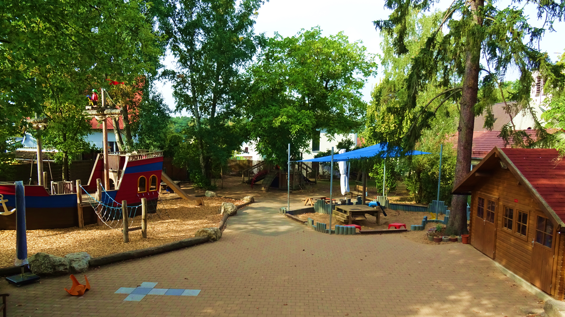 Blick aus dem Kindergarten Regenbogen in den Garten mit Piratenschiff und Sandspielplatz